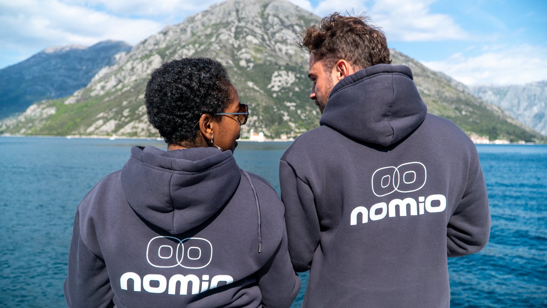 Two Nomio community members in Nomio hoodies overlooking the Bay of Kotor from a boat
