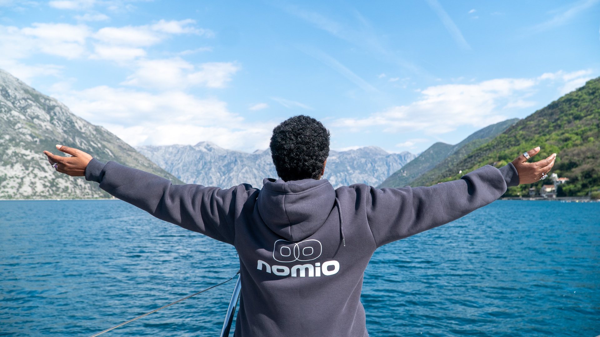 A Nomio community member opening her arms toward the mountains across the Bay of Kotor